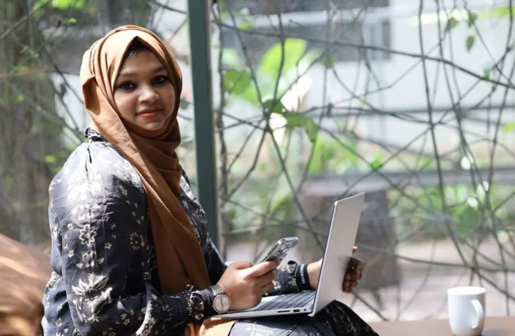 Freelance digital marketer in Malappuram working on a laptop while using a phone and having a cup of coffee.